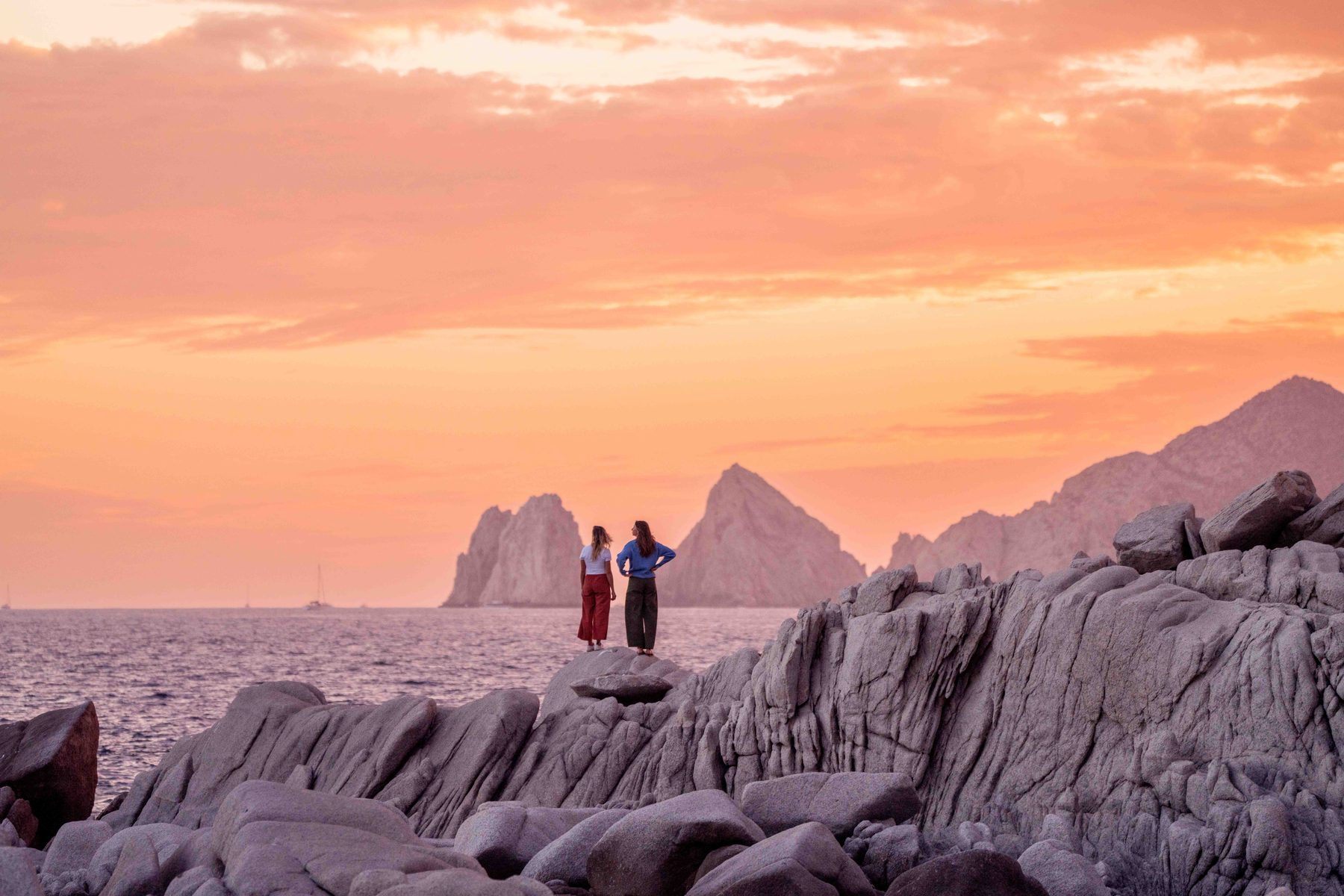 Two figures silhouetted on the rocks at Land's End at sunset